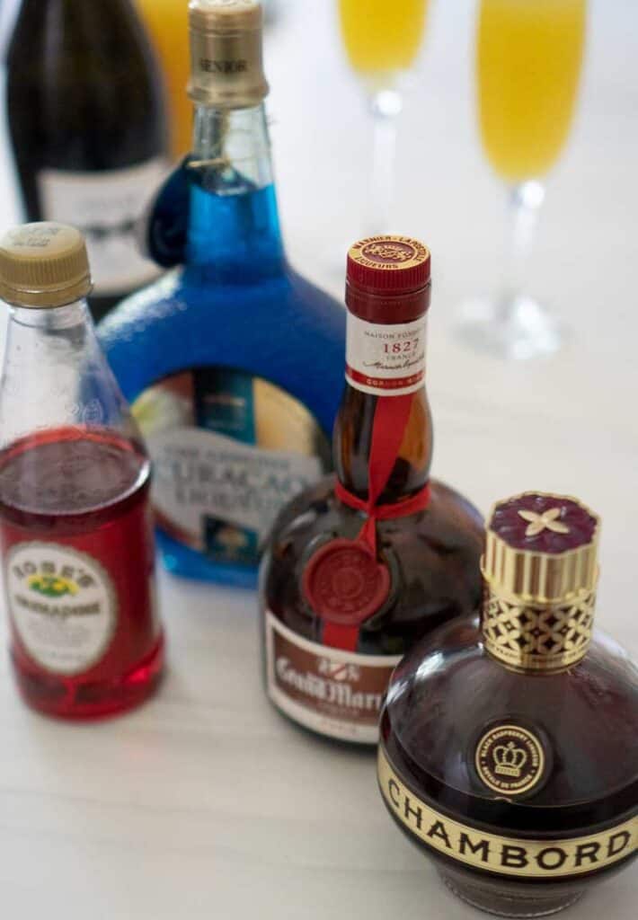 grand marnier grenadine chambord blue curacao bottles on white marble with mimosas champagne orange juice
