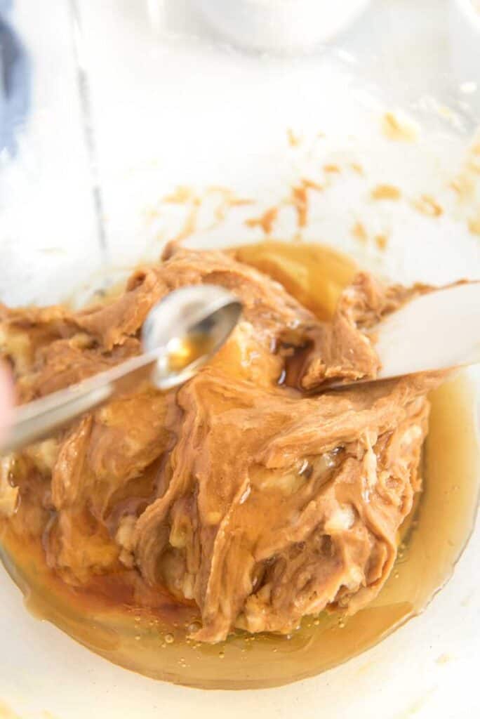 measuring spoon adding vanilla extract to peanut butter cookie dough in glass bowl