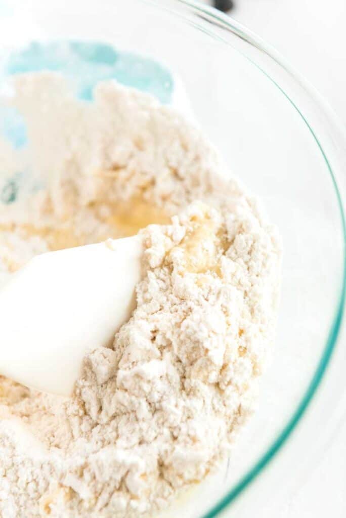 spatula mixing blueberry muffin batter in glass bowl