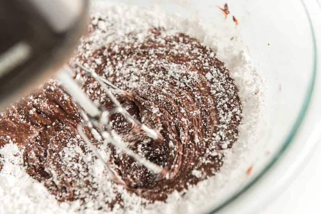 mixer mixing chocolate frosting in glass bowl