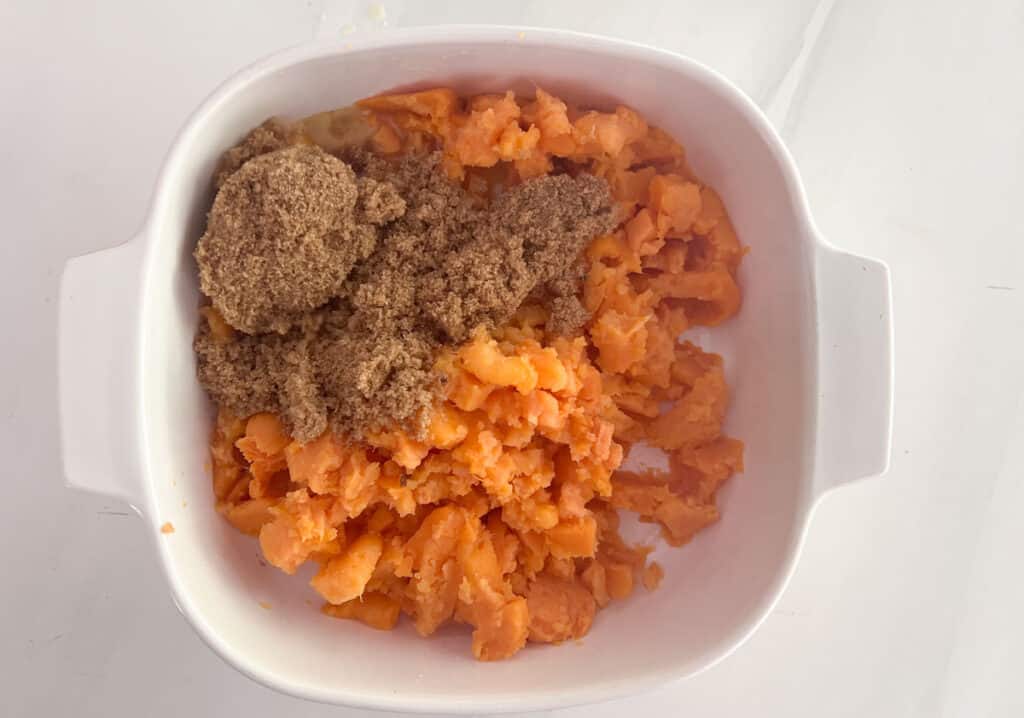 mashed sweet potatoes in white baking dish with brown sugar