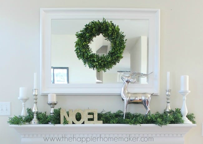 A close up of a mirror with a box tree wreath centered and silver accents with the word NOEL on the mantle