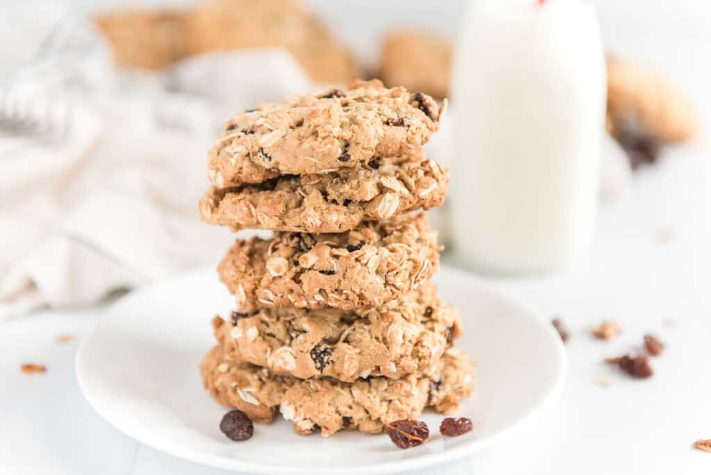 five oatmeal raisin cookies stacked on one another with milk in the background in glass