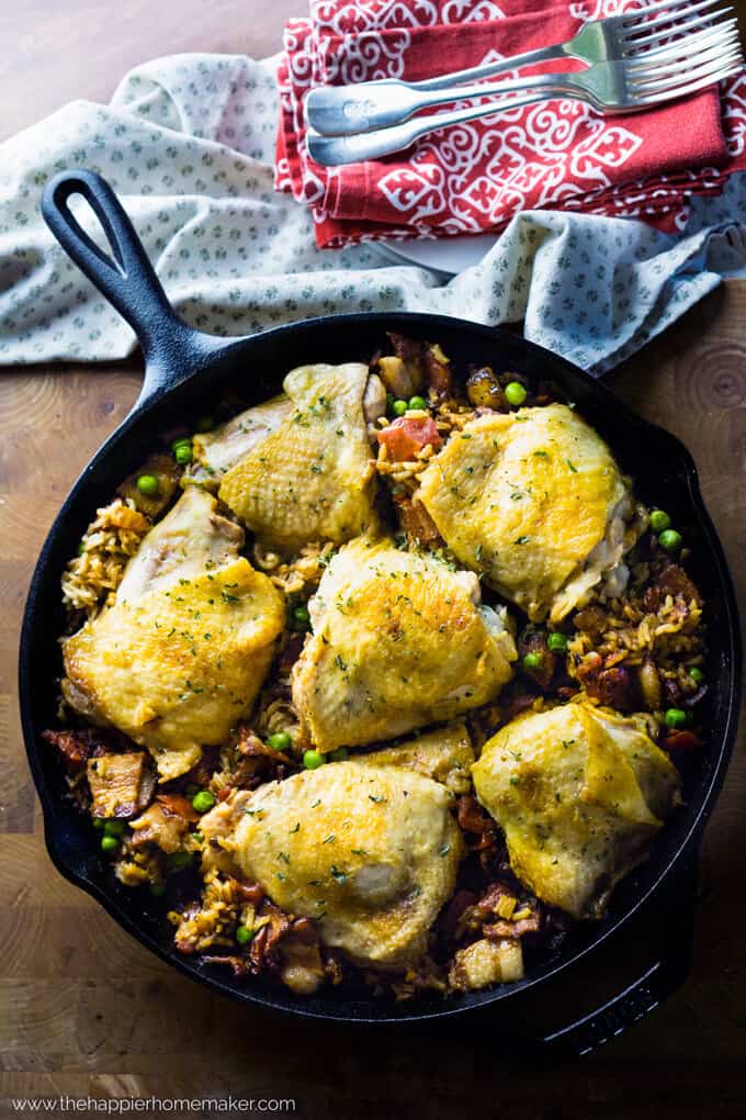 A cast iron pan full of Spanish rice chicken with kitchen towels in the background