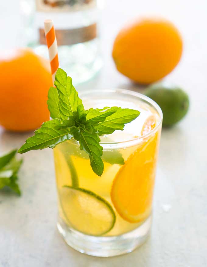 glass of orange mojito with mint garnish and orange and white striped straw