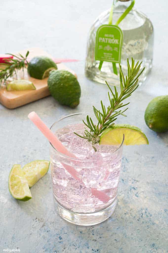 paloma cocktail in short glass garnished with lime slice and rosemary in front of tequila bottle and limes
