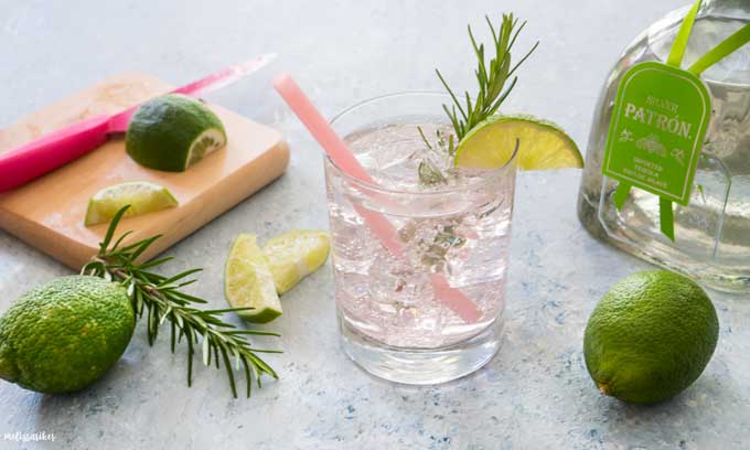 close up of paloma cocktail garnished with lime and rosemary with pink straw