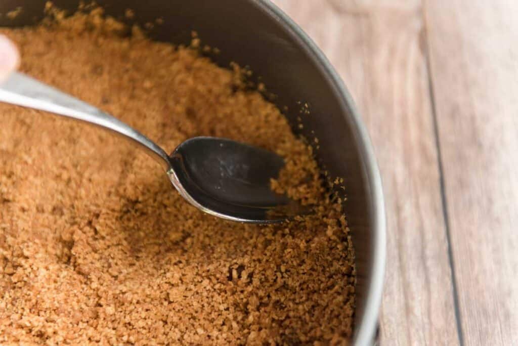 spoon pressing graham cracker crust into bottom of pan
