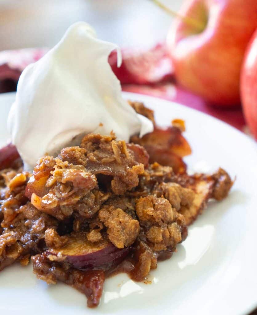 peanut butter apple crisp on white plate with whipped cream on top