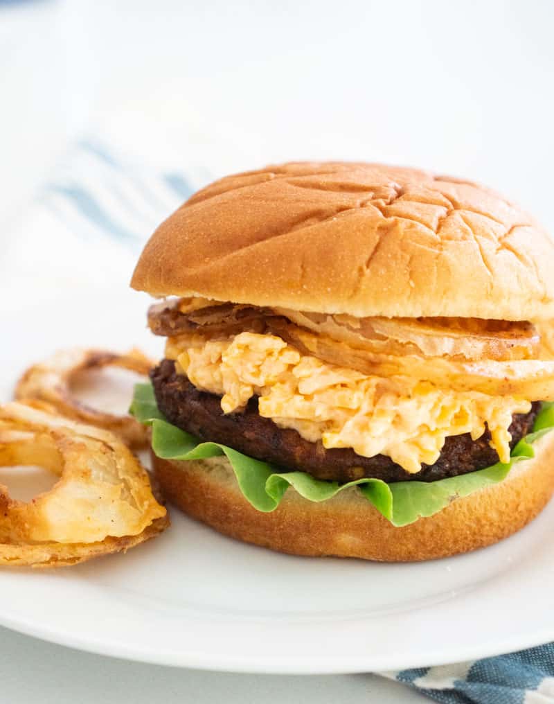 spicy black bean burger with pimento cheese and homemade fried onions on bun with lettuce on white plate