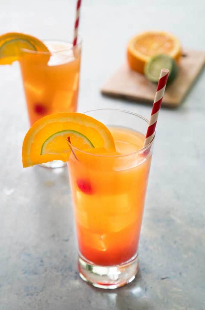 two glasses of planters punch cocktail with red and white straws