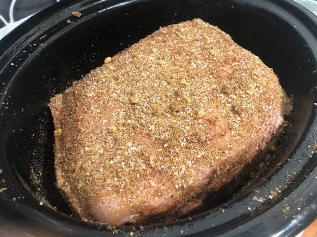 seasoned pork shoulder in slow cooker before cooking