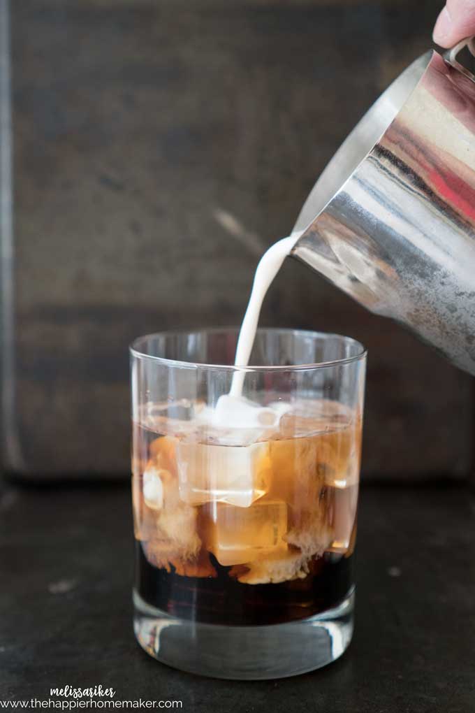 A silver pitcher pouring a pumpkin spice white russian drink into a glass 