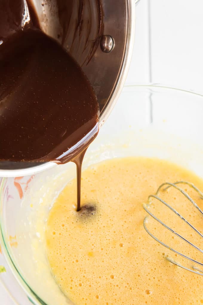 pouring chocolate from saucepan into glass bowl with batter