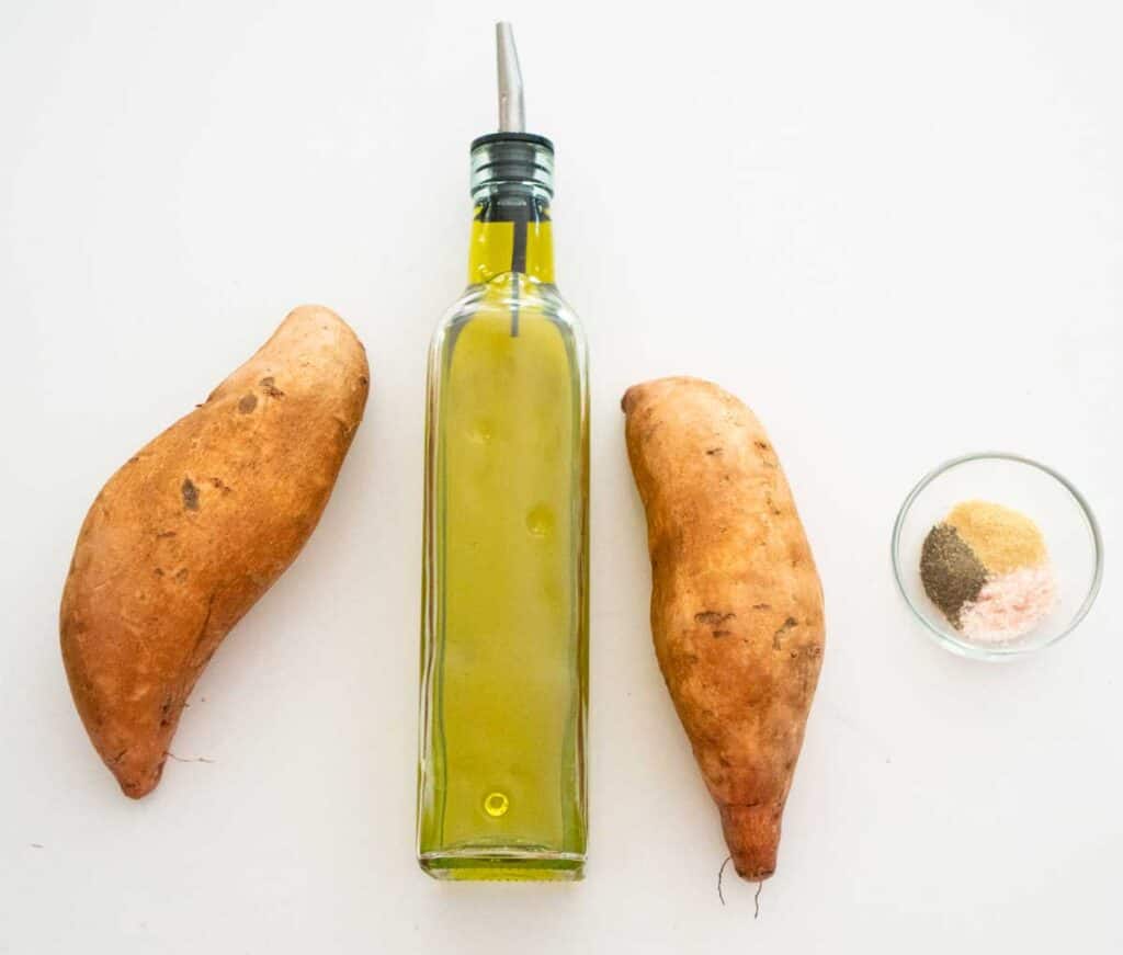 two sweet potatoes, olive oil bottle, and small glass bowl with spices