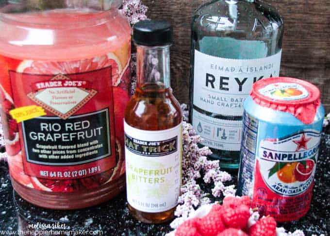 A collection of ingredients to make ruby red raspberry cocktail including bitters, red grapefruit and raspberries