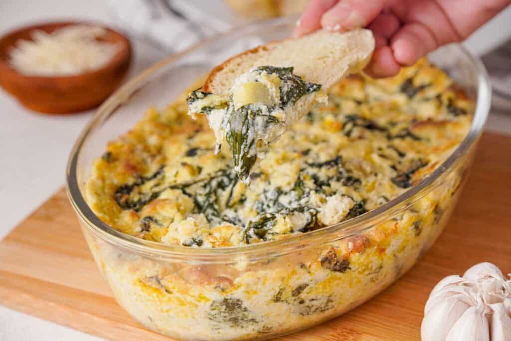 hand scooping spinach artichoke dip on crusty bread