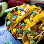 Three soft chicken tacos topped with avocados and peppers