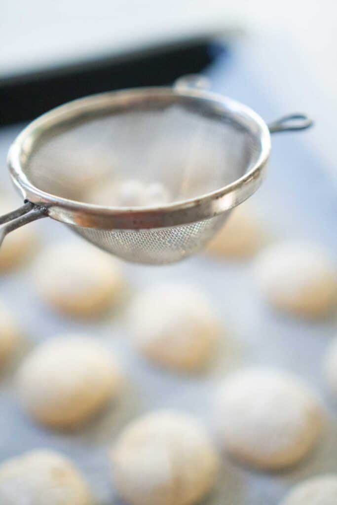 sifter held over cookies on baking sheet