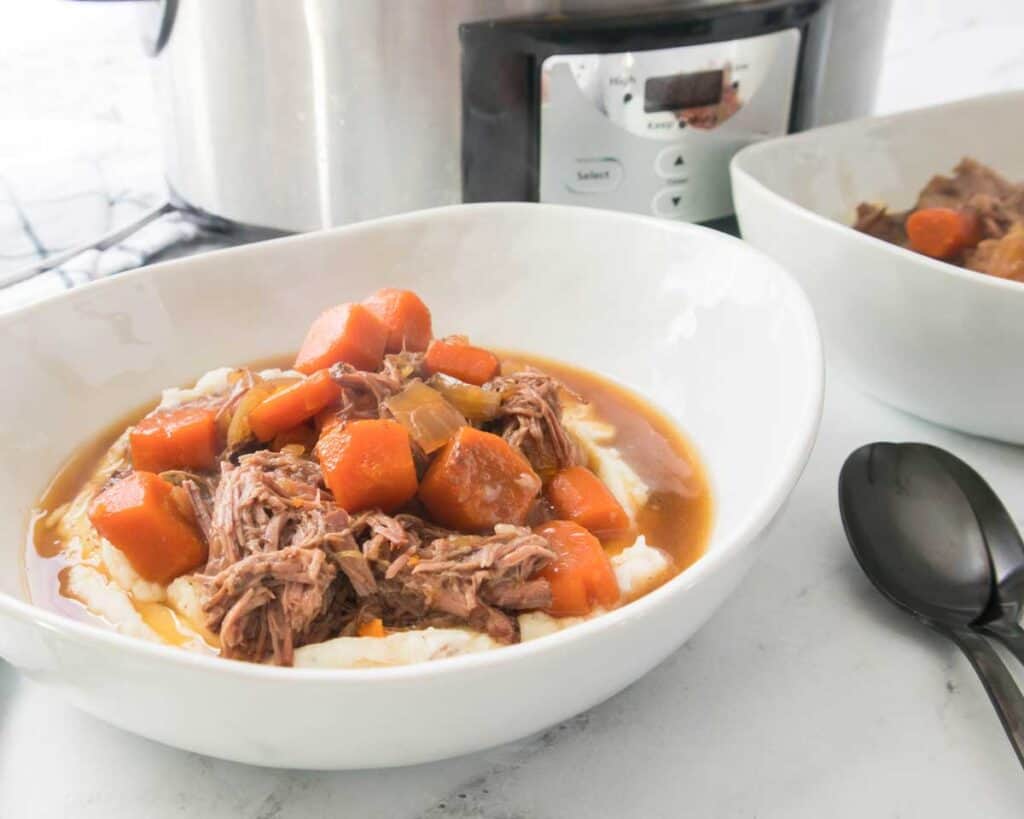 white bowl with mashed potatoes and pot roast with slow cooker in background