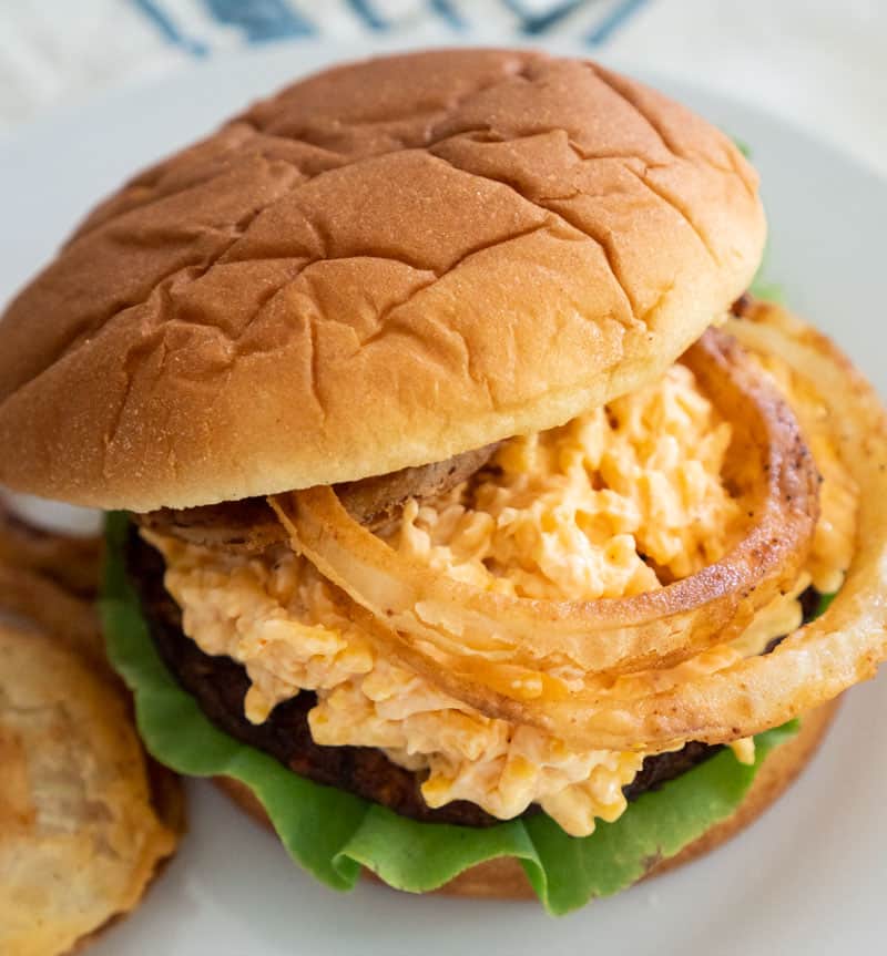 spicy black bean burger with pimento cheese and homemade fried onions on bun with lettuce on white plate