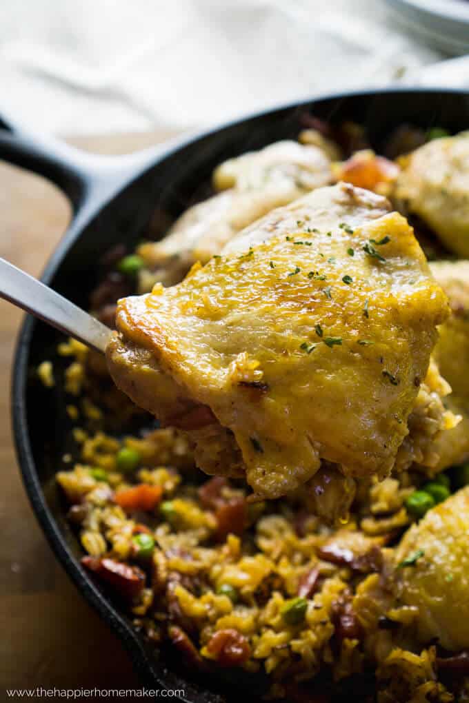 Spanish chicken in a spoon held over a cast iron skillet with rice