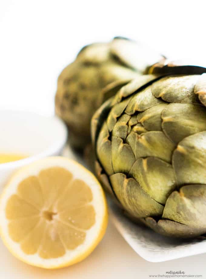two artichokes with a halved lemon and butter sauce