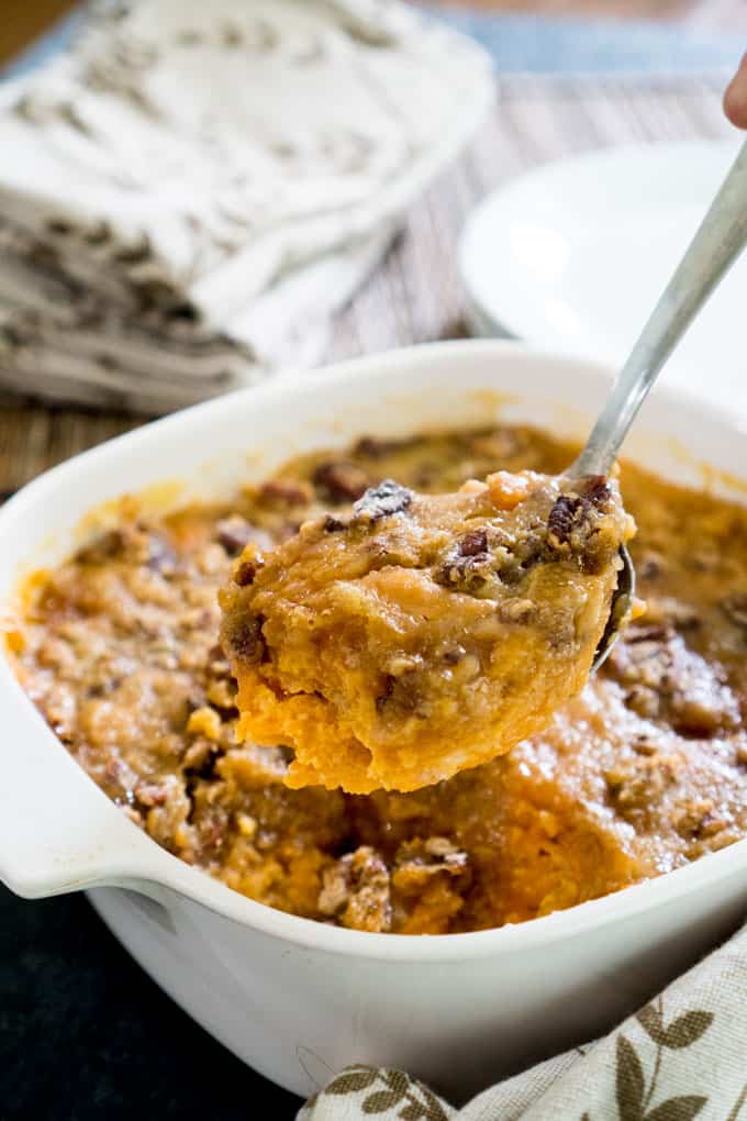 sweet potato casserole in serving spoon in front of casserole dish