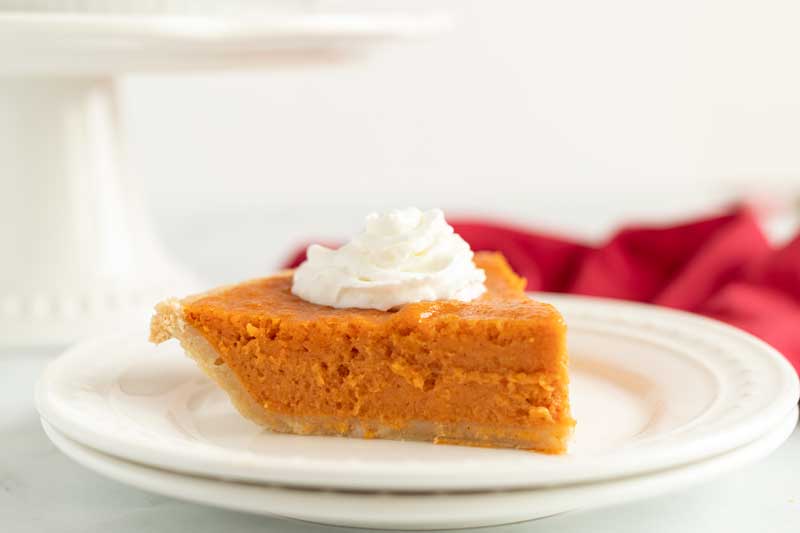 slice of sweet potato pie with whipped cream on white plate