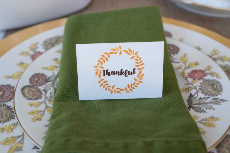 autumn themed china setting with green napkin and place card that says thankful inside an orange wreath