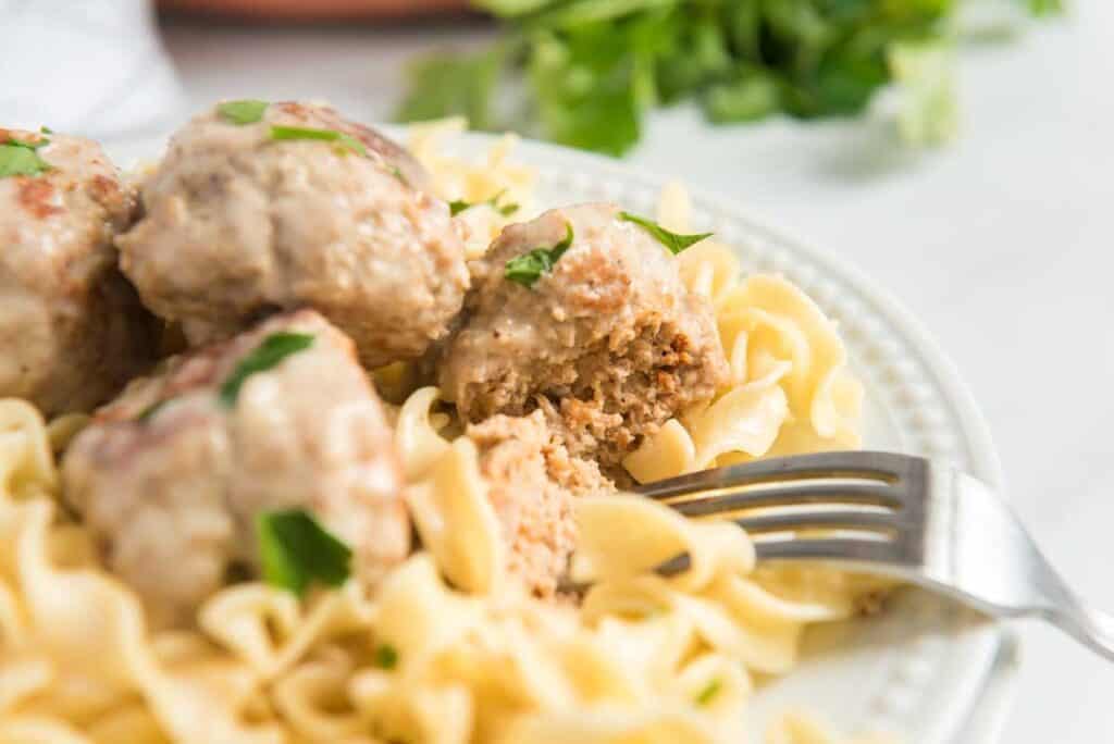 fork cutting Swedish meatball over egg noodles