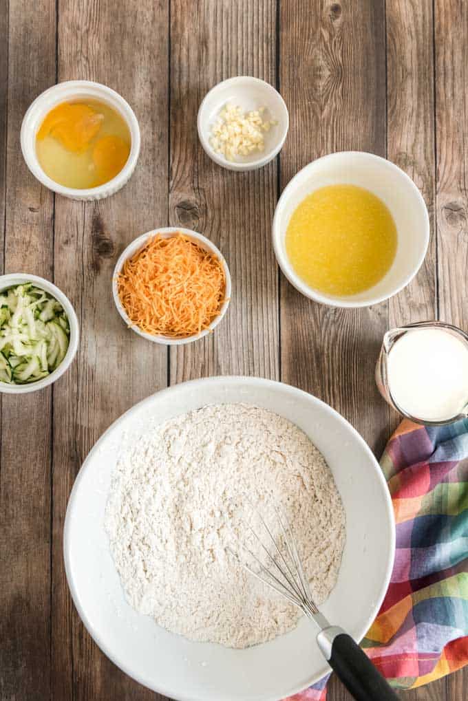 overhead photo of ingredients for cheddar zucchini bread in white bowls on wood plank background