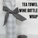 A glass of red wine next to wine bottle wrapped in tea towel